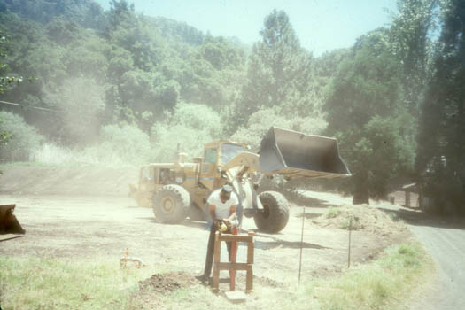 Lou Bordi working on a fire hydrant support while his operators work on the subgrade for the parking lot. The construction of the parking lot was a big deal and major advance as prior to that everyone sort of parked here and there and on down the road into the nursery and down towards below the main farmhouse. The parking lot was done during the construction on the new water system.